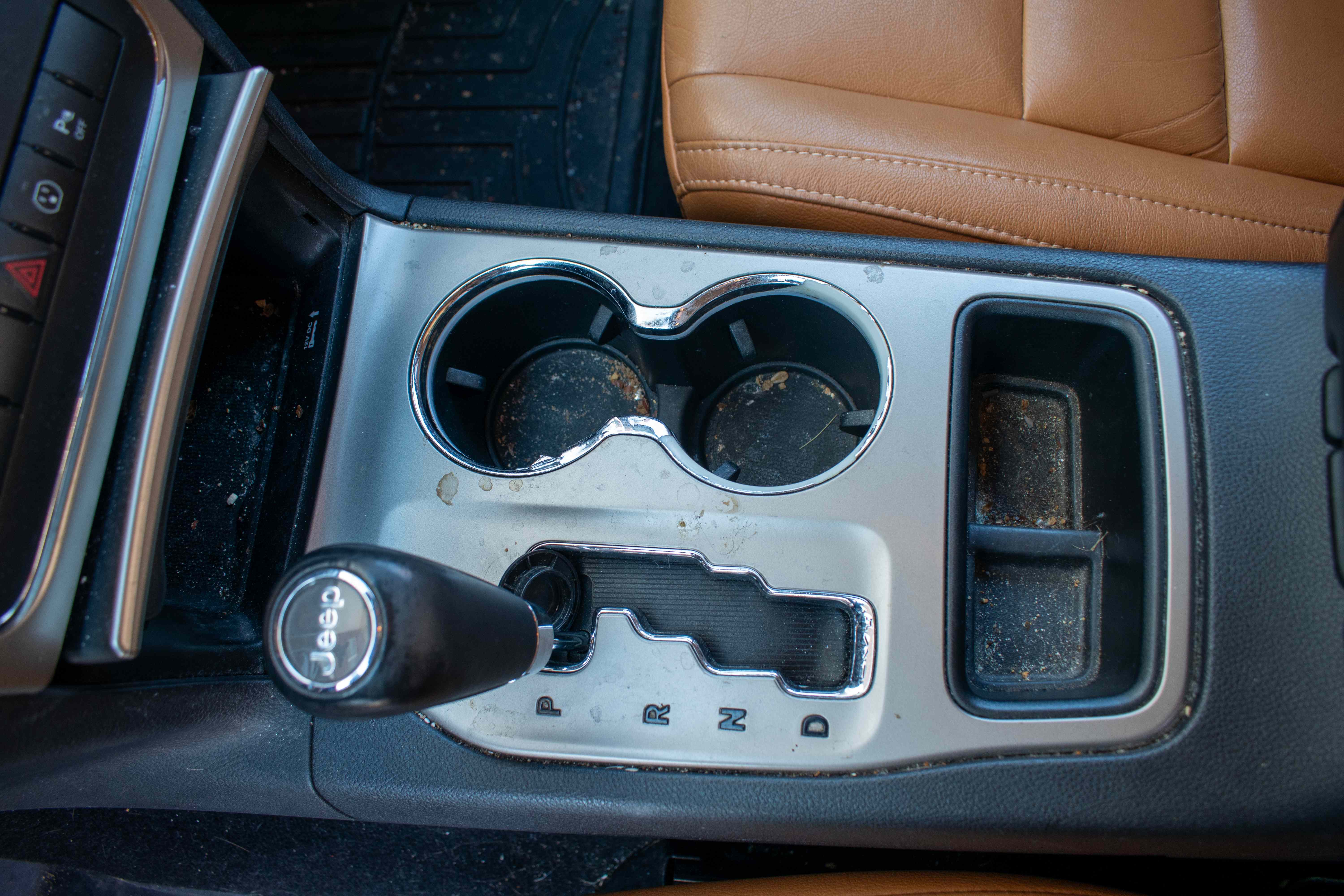 Dirty tan-seat vehicle center console with crumbs and spills before interior detailing