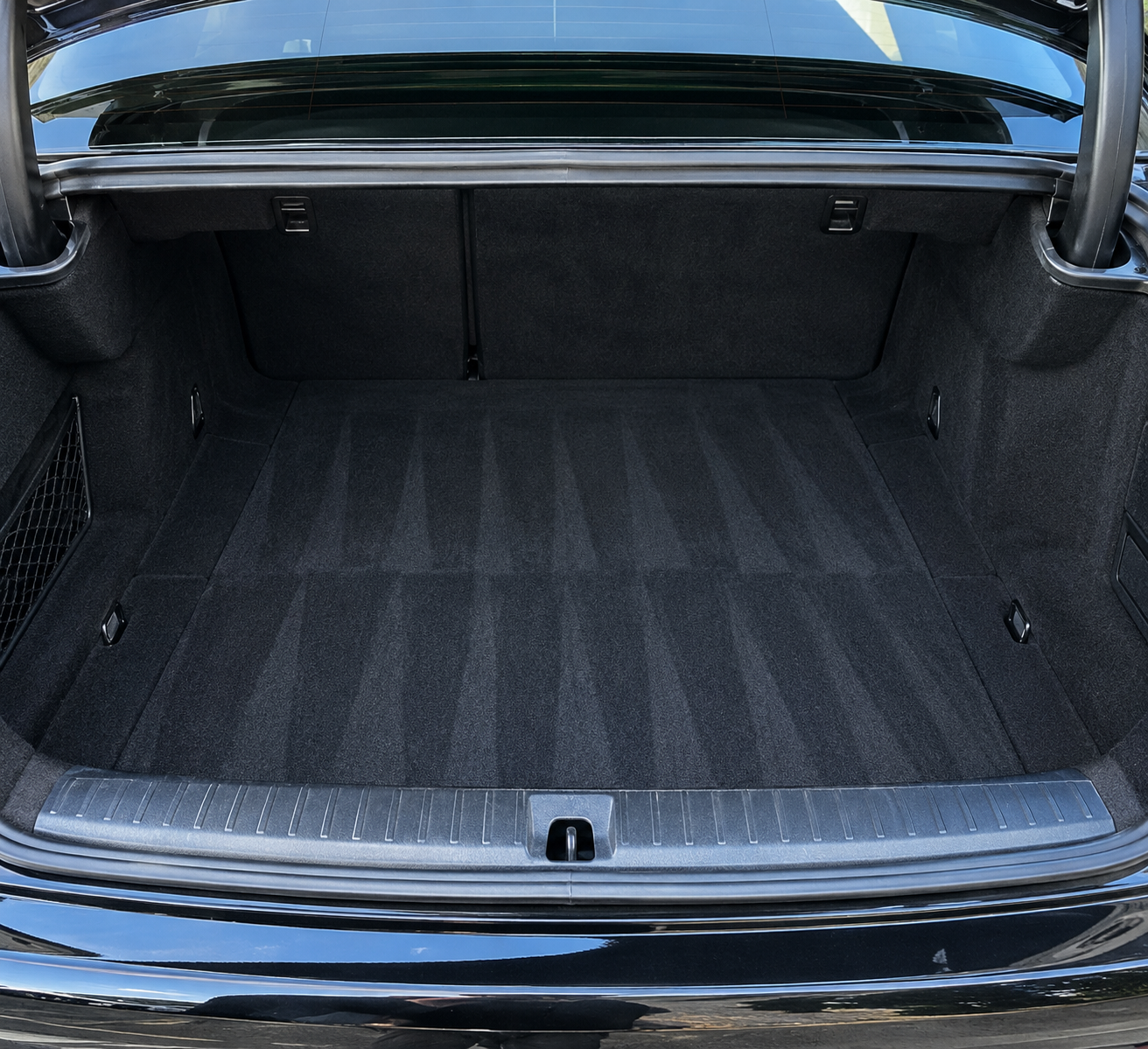 Spotless rear cargo area with freshly detailed dark carpeting and blue reflections across the trunk opening.
